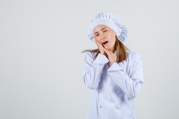 Chef feminina sofrendo de dor de dente, vestida de uniforme branco e parecendo dolorida