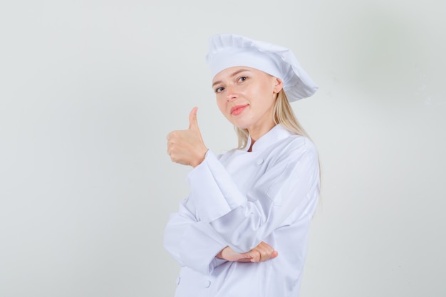 Chef feminino aparecendo o polegar em uniforme branco e parecendo alegre.