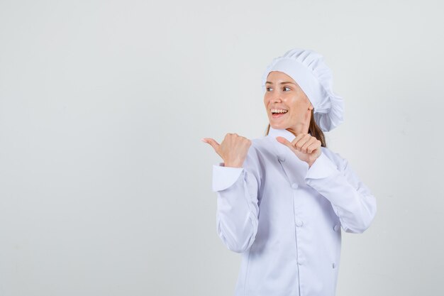 Chef feminino apontando os polegares para o lado em uniforme branco e parecendo alegre.