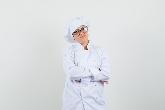 Chef feminino em pé com os braços cruzados em uniforme branco e parecendo sensato.