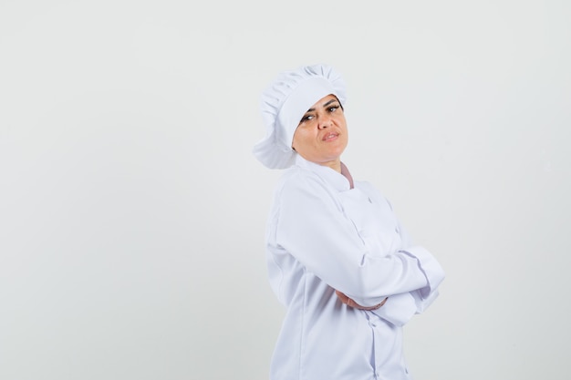 Chef feminino em uniforme branco em pé com os braços cruzados e parecendo confiante.