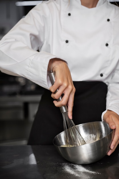 Foto grátis chef feminino na cozinha batendo ovos com batedor