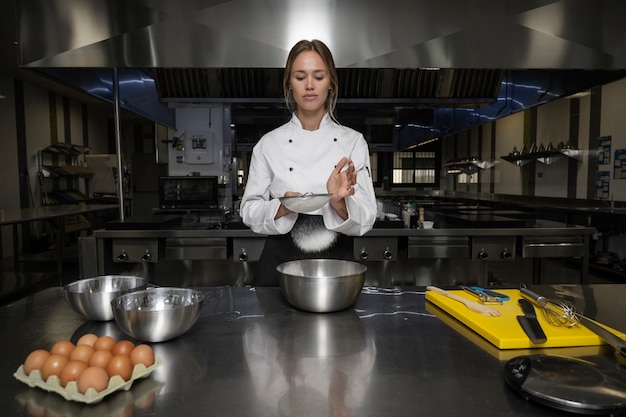 Chef feminino na cozinha peneirando farinha na tigela