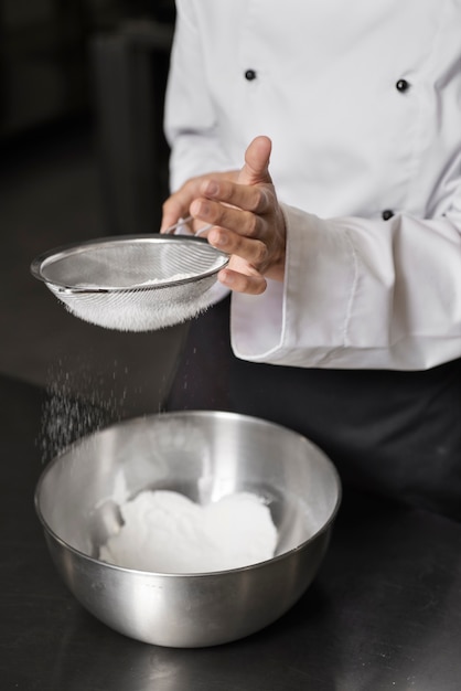 Chef feminino na cozinha peneirando farinha na tigela