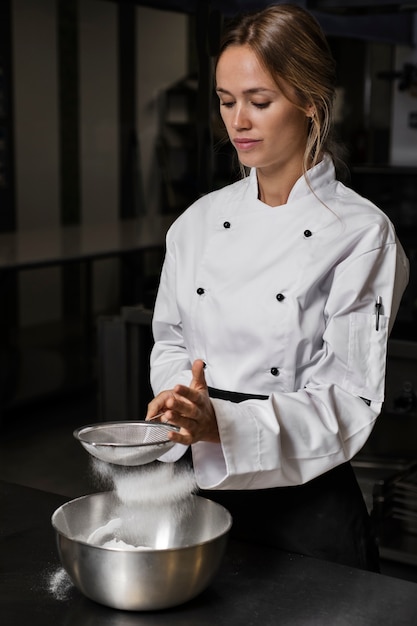 Chef feminino na cozinha peneirando farinha na tigela