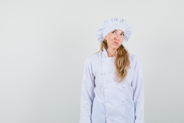 Chef feminino olhando para cima enquanto franzia a testa no uniforme branco e parecendo indeciso.