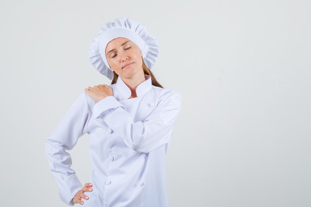 Chef feminino segurando as mãos no ombro e cintura em uniforme branco e parecendo cansado. vista frontal.