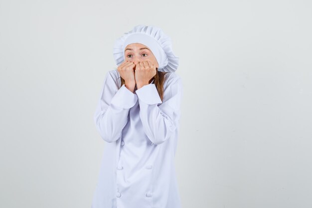 Chef feminino segurando os punhos na boca em uniforme branco e parecendo assustado. vista frontal.