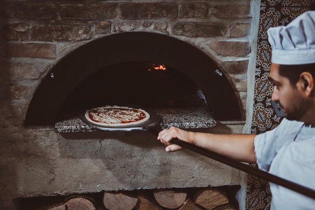 Chef italiano está colocando pizza gourmet recém-feita no forno de pedra.