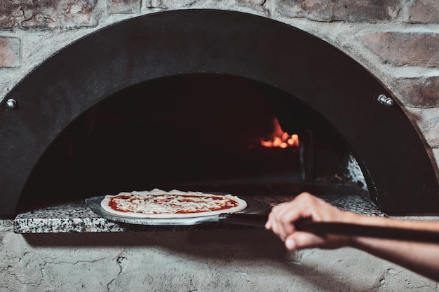 Foto grátis chef italiano está colocando pizza margarita preparada no forno com chama.