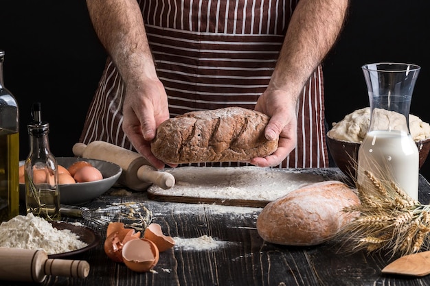 Chef mantém o pão fresco na mão. Homem preparando massa na mesa na cozinha. Em fundo preto. Conceito saudável ou cozinhar.