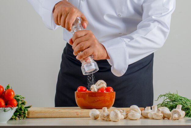 Chef masculino, adicionando sal em alimentos na cozinha de uniforme e avental