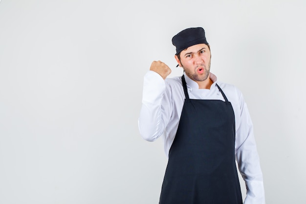 Foto grátis chef masculino aparecendo o punho cerrado no uniforme, avental e parecendo indignado. vista frontal.