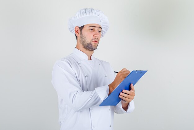 Chef masculino com uniforme branco fazendo anotações na área de transferência e parecendo ocupado