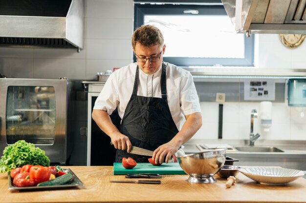 Chef masculino cortando tomates na cozinha