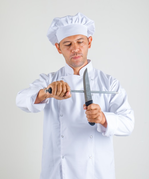 Foto grátis chef masculino cozinhar de uniforme e chapéu segurando facas de cozinha e olhar confiante