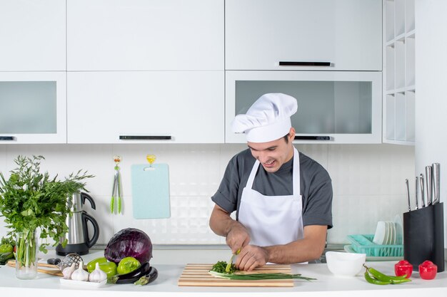 Chef masculino de uniforme cortando verduras atrás da mesa da cozinha