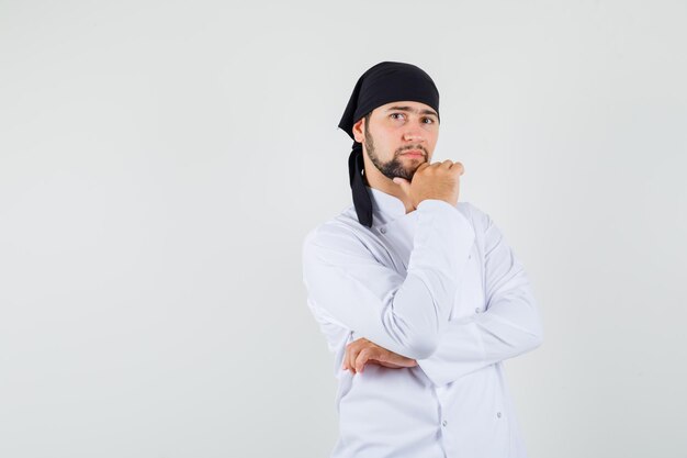 Chef masculino em pé na pose de pensamento de uniforme branco e parecendo sensato. vista frontal.