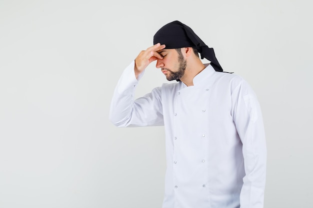 Chef masculino em uniforme branco, esfregando os olhos e o nariz e parecendo cansado, vista frontal.