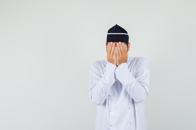 Chef masculino em uniforme branco, segurando as mãos no rosto e olhando preocupado, vista frontal. espaço para texto