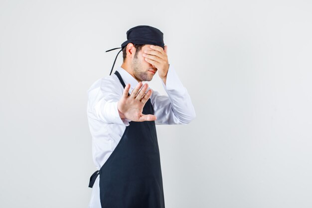 Chef masculino mostrando gesto de recusa com os olhos cobertos de uniforme, vista frontal do avental.
