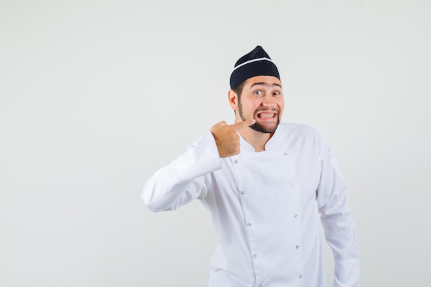 Chef masculino mostrando os dentes em uniforme branco e bonito, vista frontal.