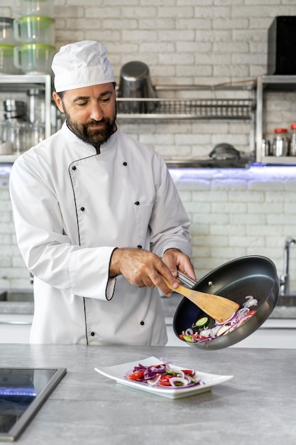 Foto grátis chef masculino na cozinha derramando comida no prato da frigideira