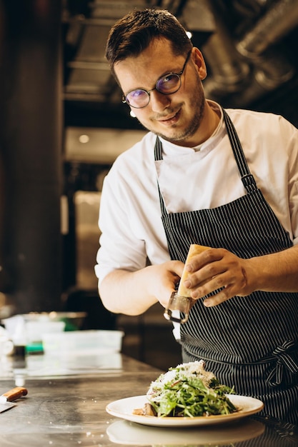 Chef masculino na cozinha preparando salada esfregando queijo em cima