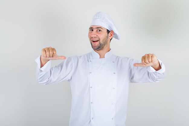Chef masculino se mostrando com polegares em uniforme branco e parecendo orgulhoso.