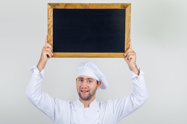 Foto grátis chef masculino segurando a lousa aérea em uniforme branco e olhando positivo.