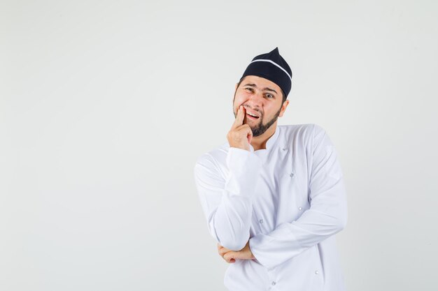 Chef masculino sofrendo de dor de dente em uniforme branco e olhando com problemas, vista frontal.