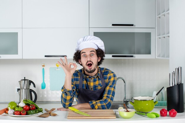 Chef masculino sorridente com legumes frescos fazendo gesto de óculos na cozinha branca