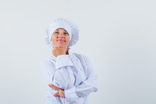 Chef mulher apoiando o queixo no punho em uniforme branco e parecendo sensato.