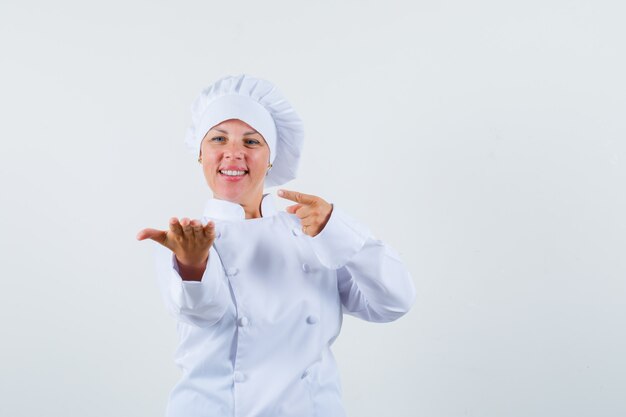 chef mulher apontando para algo na mão em uniforme branco e olhando focado.