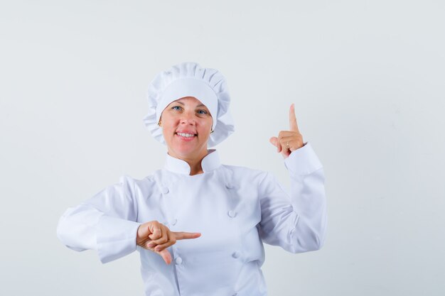 chef mulher apontando para o lado e para cima em uniforme branco e parecendo confiante.