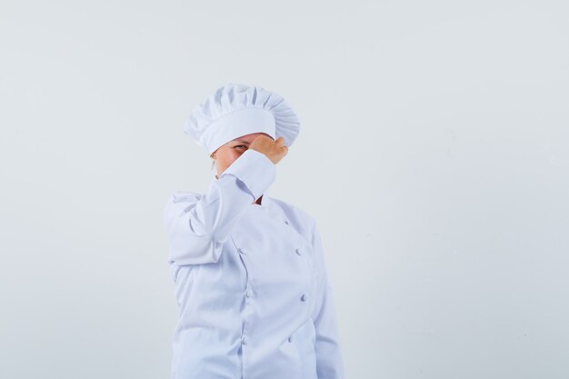 chef mulher beliscando o nariz em um uniforme branco e parecendo preocupada