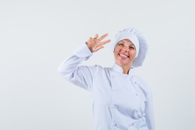 Chef mulher com uniforme branco mostrando o sinal em V e parecendo alegre