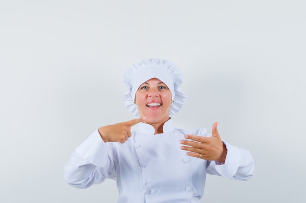Foto grátis chef mulher de uniforme branco apontando para o lado, fingindo estar segurando algo e parecendo confiante