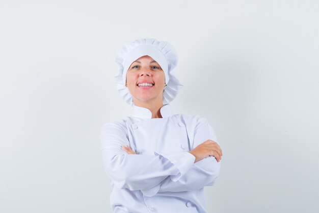 Chef mulher de uniforme branco em pé com os braços cruzados e parecendo confiante