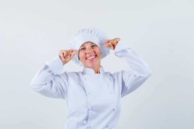 Foto grátis chef mulher mostrando sinal de tamanho pequeno em uniforme branco e olhando positivo.