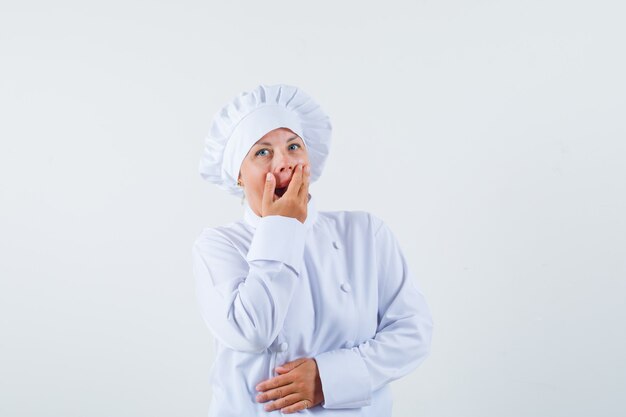 chef mulher segurando a boca com a mão em um uniforme branco e parecendo pasma