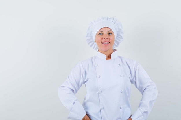 Chef mulher segurando as mãos na cintura em um uniforme branco e parecendo confiante