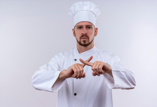 Chef profissional cozinheiro de uniforme branco e chapéu de cozinheiro fazendo gesto de defesa cruzando os dedos indicadores em pé sobre um fundo branco