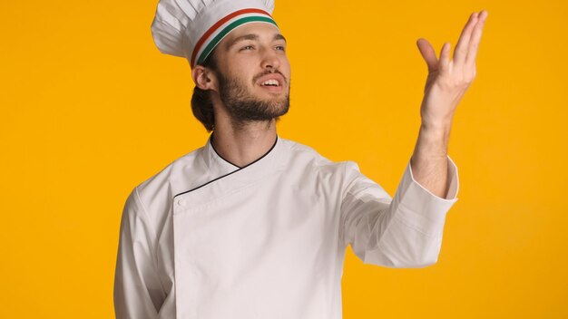 Chef profissional mostrando um gesto delicioso usando uniforme isolado em fundo colorido Homem atraente com chapéu de chef olhando inspirado posando para a câmera no estúdio