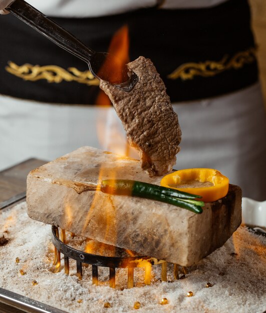 chef segurando bife na pedra com pimentos grelhados em chamas