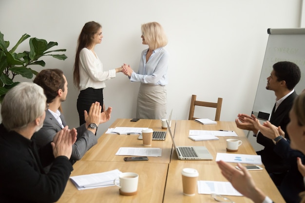 Chefe de mulher de negócios sênior, promovendo agradecendo a funcionária enquanto equipe aplaudindo