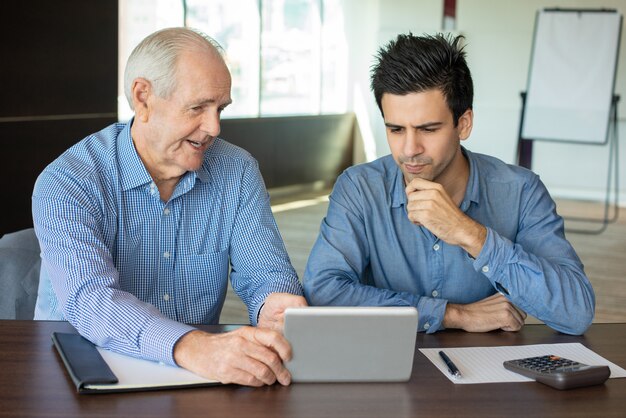 Chefe sênior, mostrando dados para jovem empregado no tablet