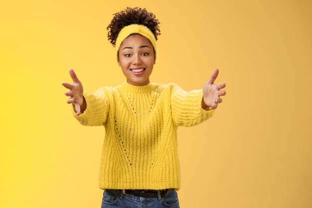 Foto grátis chegue mais perto, deixe-me te abraçar. tocada linda feliz jovem bonita afro-americana estender os braços quer segurar os braços de bebê fofo encantador pedindo abraço abraço amigável, posando com fundo amarelo.