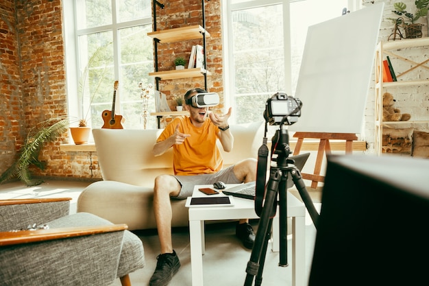 Cheio de emoções. Blogueiro do sexo masculino, caucasiano, com câmera profissional gravando análise de vídeo de óculos de realidade virtual