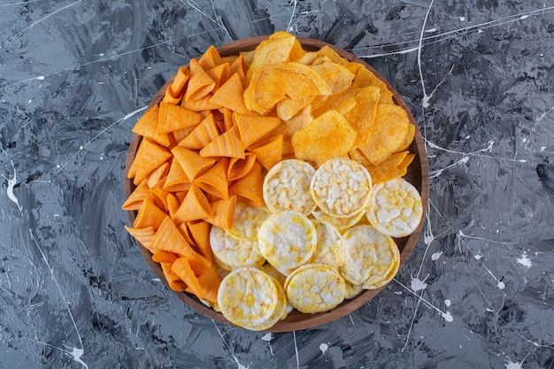 Chips de queijo, batata frita e chips de cone em placa de madeira, na superfície de mármore